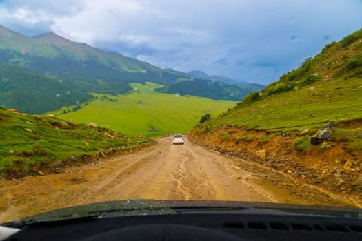 cars driving down the dirt road at rainy summer day in mountains, view from drivers perspective.
