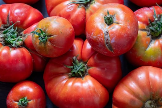 A bunch of red tomatoes are piled on top of each other. The tomatoes are all different sizes and shapes, but they all have a similar color. Concept of abundance and freshness, as the tomatoes are ripe