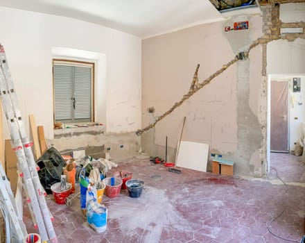 An unfinished room during a home renovation with construction tools, materials, and a ladder scattered around. Exposed brick and plaster walls under reconstruction
