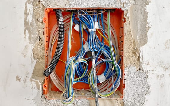 Close-up view of exposed electrical wiring and conduits inside a wall during renovation, showing colorful cables and installation details
