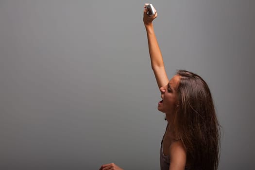 Young woman screams in joy, holding a smartphone above her head in celebration of good news, exuding pure excitement and happiness