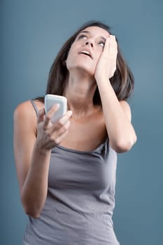 Stressed woman holding phone indoors against blue and gray background, looking up with frustration and concern, facing communication issues