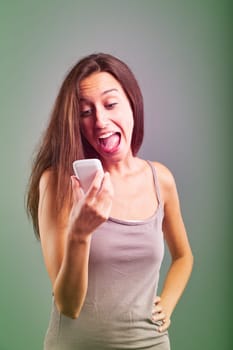 Surprised young woman is holding a smartphone in her hand, sticking her tongue out and reading a text message with a funny expression on her face