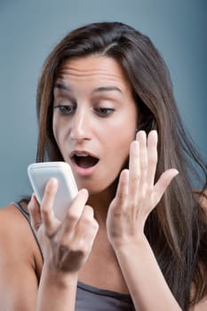 Surprised woman holding smartphone, reacting to shocking content, against blue background. Expression conveys disbelief and wonder. Browsing internet, amazed by message