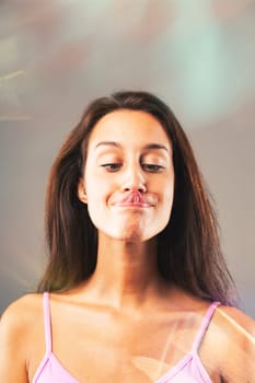 Young woman playfully sticks out her tongue and makes a funny face, exuding joy in a pink top with long brown hair