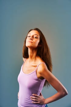 Confident young woman posing stylishly in studio with hands on hips, exuding self assurance and femininity against blue background