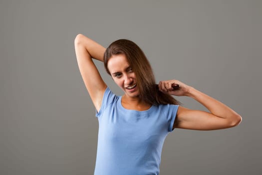 Frustrated young woman pulls at her long brown hair, showing anger, stress, and worry against a gray background