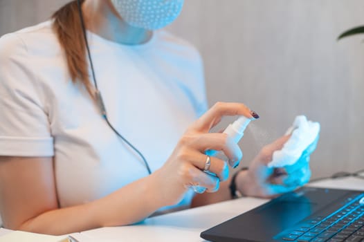 Woman disinfects the surface of the phone by sanitizer spray on the working place.