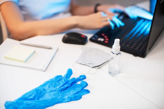 Woman in mask, working from home. Sanitizer anti virus spray on the working table. Coronavirus, quarantine for COVID-19 concept.