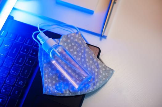 Sanitizer anti virus spray and protective mask on the working table with laptop. Personal hygiene concept. Concept of quarantine for coronavirus and working from home.
