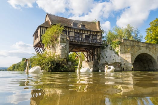 The beautiful old mill on the broken bridge over Seine river with swans in the foreground in Vernon, Normandy, France