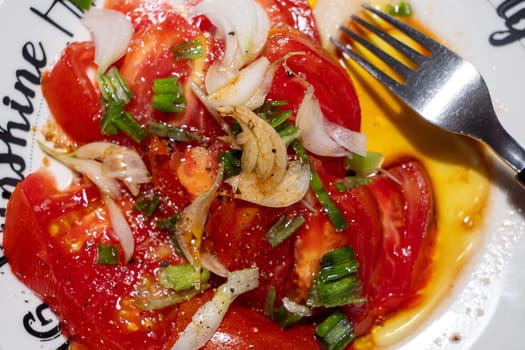 A plate of food with a fork on it. The plate has a white background and the food is a mix of tomatoes and onions