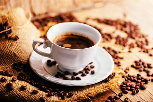 Closeup of coffee cup and coffee beans with vintage burlap on rustic wooden table. Hot beverage in mug still life. Cafe restaurant shop creative menu background.