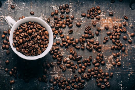 Top view of coffee cup on coffee bean texture and black rustic background. Hot beverage on vintage dark table. Restaurant cafe shop creative menu.