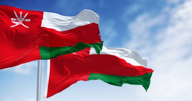 National flags of Oman waving in the wind on a clear day. Vertical red stripe with Oman emblem and three horizontal stripes: white, red, and green. 3d illustration render. Rippling fabric