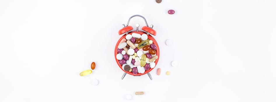 Nutritional supplement color pills on red alarm clock face isolated on white background with copy space. Template for feminine beauty blog social media. Female healthcare concept