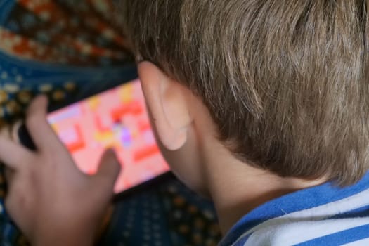 A boy is playing a game on his phone. The game is colorful and has a maze-like design