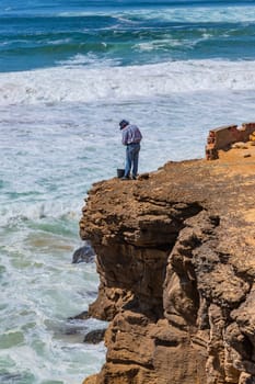 Sintra, Portugal: April 13, 2024: A fisherman stands on the edge of a cliff by the ocean in Ericeira, Portugal