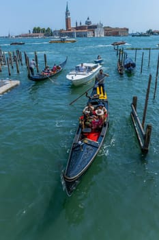 Venice, Italy - July 26, 2024: Gondolas against the San Giorgio island in Venice, Italy. Gondola is the most attractive tourist transport in Venice. Traveling and vacation in sunny Venice.