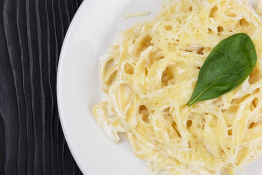 Pasta with sauce and basil in plate on black wooden background