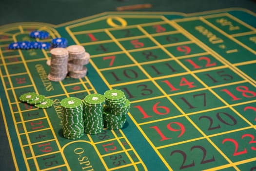 Casino, gambling and entertainment concept - green roulette table with colored chips ready to play