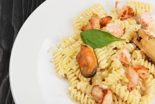 Seafood Pasta with mussels salmon and shrimps with basil in white plate on black wooden background.