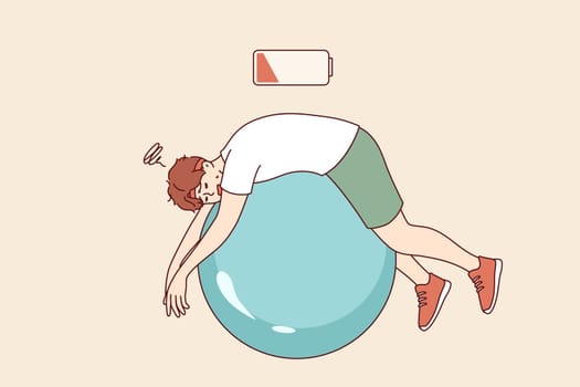 Tired man lies on fitness ball with empty battery, symbolizing exhaustion and lack of vitality. Tired guy being lazy doing pilates to improve health or get rid of illnesses and excess weight