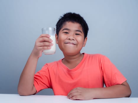 Concept of happy good nutrition, Portrait of a little young handsome kid boy in pink t-shirt, Holding a glass of milk on white background, Smiling of Asian boy with a glass of milk.