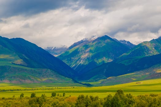 Embrace and enjoy a stunning and breathtaking view of majestic mountains and lush green valleys beneath a dramatic sky in Kyrgyzstan