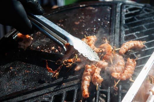 A professional cook prepares shrimps on the grill outdoor, food or catering concept