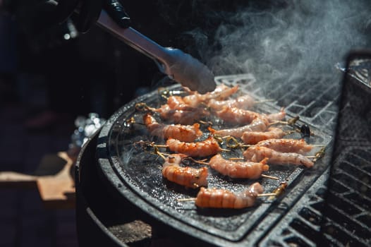 A professional cook prepares shrimps on the grill outdoor, food or catering concept