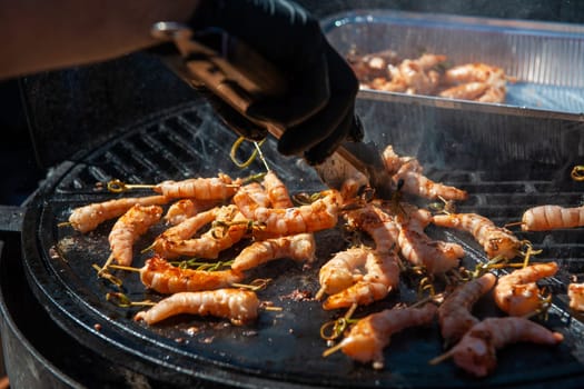 A professional cook prepares shrimps on the grill outdoor, food or catering concept