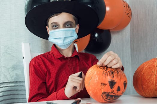 Teen boy in costume and face masks to protect against COVID-19 drawing a pumpkin for the Halloween celebration. Halloween carnival with new reality with pandemic concept.