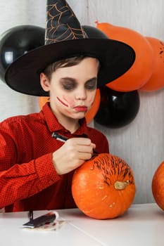 Happy teen boy in costume preparing for the Halloween celebration drawing a pumpkin. Halloween carnival or masquerade concept