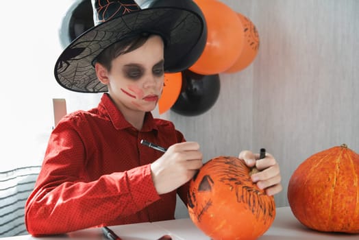 Happy teen boy in costume preparing for the Halloween celebration drawing a pumpkin. Halloween carnival or masquerade concept