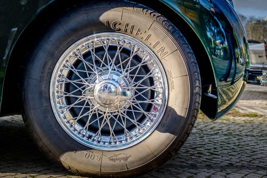 Lisbon, Portugal - Jan 20, 2024: Car design detail of Jaguar chrome wire wheel, stainless steel spokes, polished and chrome-plated with signs of wear-and-tear and bespoke 2-eared wire wheel spinner for splined hub with Jaguar logo. Michelin tyre.