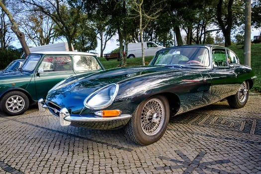 Lisbon, Portugal - Jan 20, 2024: A classic dark green E-Type Jaguar Series 1 coupe car with chrome detailing parked on a cobblestone road near green park.