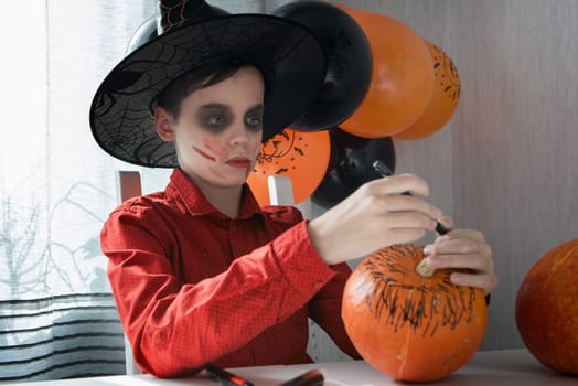 Happy teen boy in costume preparing for the Halloween celebration drawing a pumpkin. Halloween carnival or masquerade concept