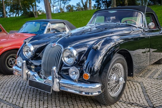 Lisbon, Portugal - Jan 20, 2024: Vintage dark green Jaguar XK150 drophead coupe car car parked on cobblestone pavement road. Two-seater roadster, sports car, convertible