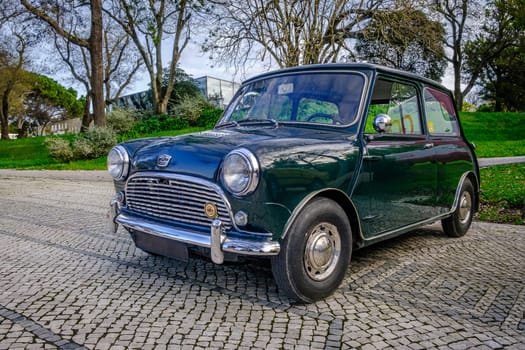 Lisbon, Portugal - Jan 20, 2024: A classic green Mark I Mini or Austin Mini Super-Deluxe car with chrome detailing parked on a cobblestone road near green park.