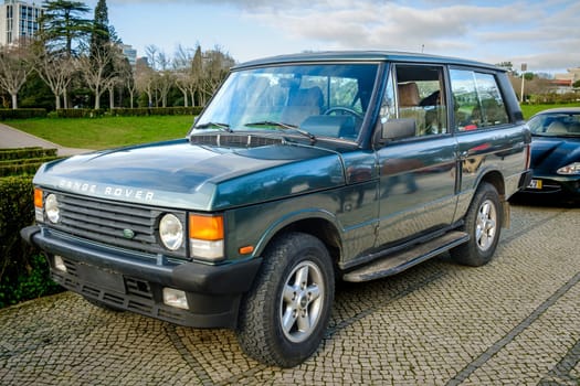 Lisbon, Portugal - Jan 20, 2024: A classic green Land Rover Range Rover car parked on a cobblestone path near green park. 4x4, mid-size off-road vehicle as two-door model of first generation.