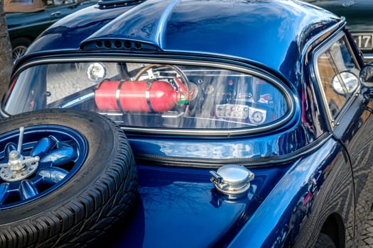 Lisbon, Portugal - Jan 20, 2024: Rear view of blue vintage sports car - a spare tyre mounted on top of trunk and red fire extinguisher inside the car behind rear window. Car interior two-seater coupe also visible.
