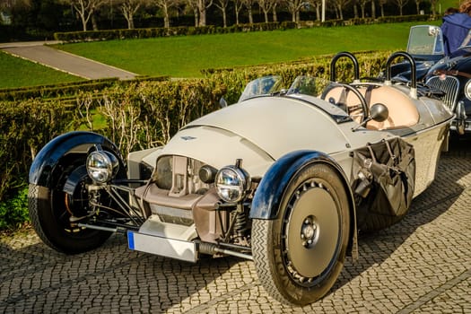 Lisbon, Portugal - Jan 20, 2024: Luxury Morgan Super 3 3-wheeled sports car without soft top parked on a cobblestone path near green park.