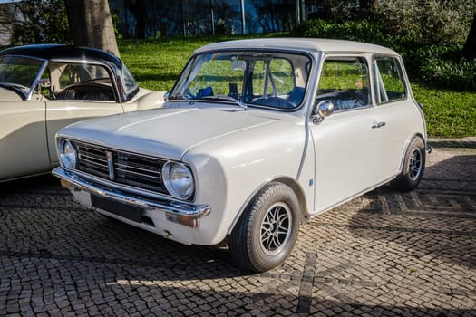 Lisbon, Portugal - Jan 20, 2024: Iconic white Leyland Mini Clubman car parked on a cobblestone road near green park. 2-door saloon car