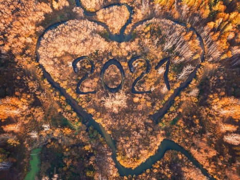 Heart shaped river in autumn forest with 2021 text as river. New year concept, aerial drone view