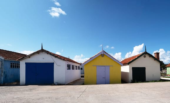 Three small houses with blue and yellow roofs sit in a parking lot. The houses are all different colors. Chateau Oleron, France