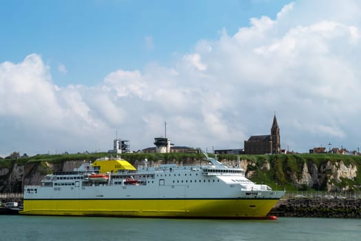 Dieppe, France, a large yellow ship is docked at the pier. The sky is cloudy and the water is calm