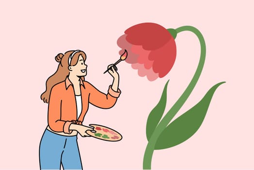 Woman artist paints flower on wall to decorate interior, uses wooden palette and brush. Positive girl artist enjoys drawing and opportunity to develop creativity and professional skills