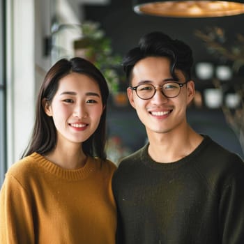 A young Chinese couple in autumnal hues shares a moment of joy in a modern cafe, their smiles as warm as their knitwear