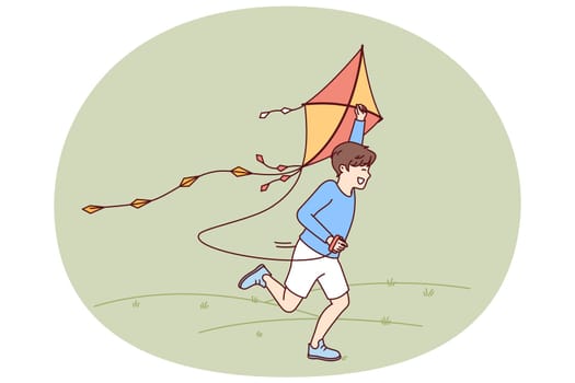 Little boy with kite runs through meadow enjoying summer walk with favorite toy. Happy kid laughing while flying kite for concept of carefree childhood and teen outdoor activity